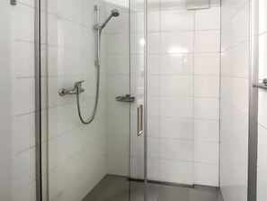 Une cabine de douche fermée par des parois en verre, équipée d’un pommeau de douche à main et d’un flexible de douche à main.