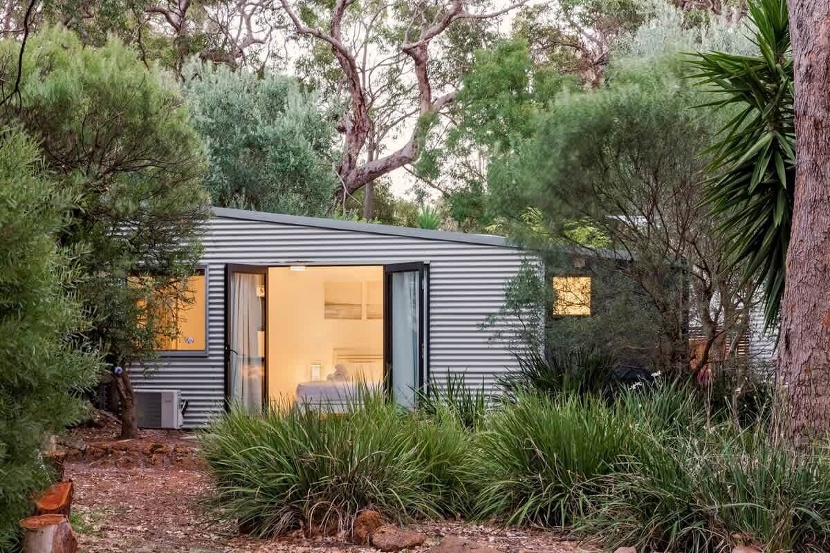 A modern, single-story building with a large sliding glass door entrance, surrounded by dense greenery and trees.