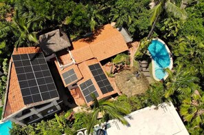 Vue aérienne d’une propriété dotée d’une piscine, de panneaux solaires et d’une structure à toit de chaume.