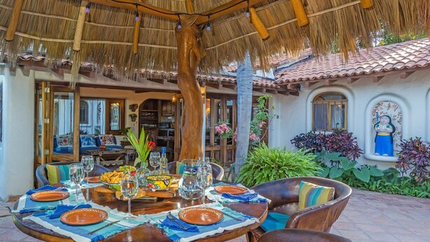 An outdoor dining area with a thatched roof, wooden furniture, and a table set for a meal.