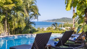 A poolside area with lounge chairs and a view of the sea.