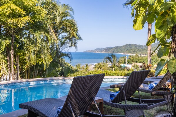 Un espace aménagé au bord de la piscine, avec des chaises longues et une vue sur la mer.
