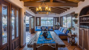 A cozy interior with a wooden ceiling, a central seating area with a patterned rug, and large windows offering views.