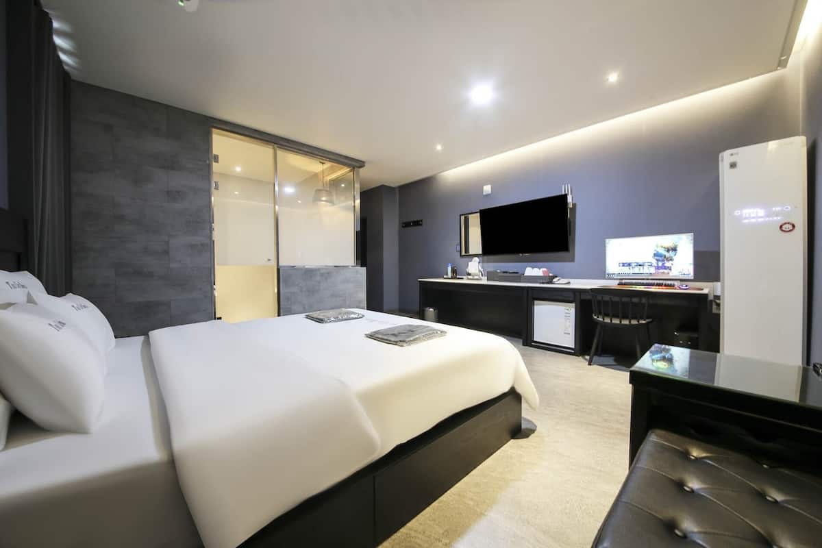 Una habitación de hotel moderna con una cama grande, un escritorio con computadora, un televisor y un minibar.