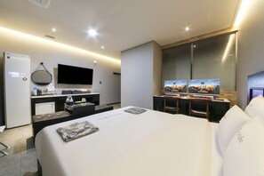 A modern hotel room with a large bed, a desk with a flat-screen TV, a minibar, and a large mirror. - The City Hotel (Nonsan)