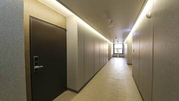 A long, narrow hallway with a dark door on the left and a window at the end.