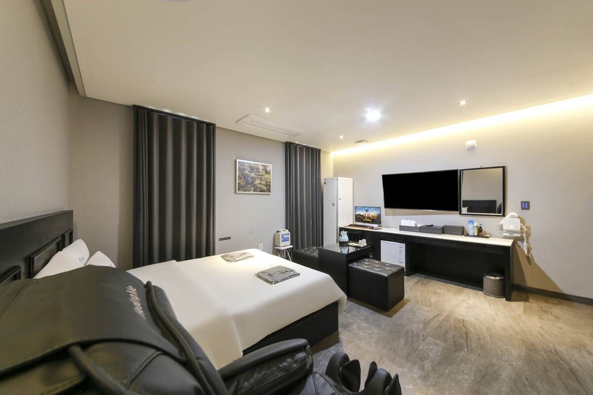 Habitación de hotel con cama, escritorio, silla, televisor y espejo.