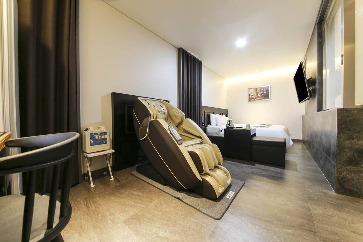 Habitación de hotel con una silla de masaje, una cama, un escritorio y un televisor de pantalla plana montado en la pared.