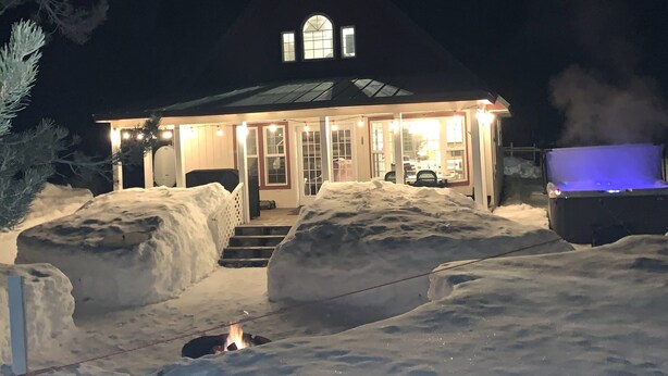 Ein mit Schnee bedecktes Haus mit Veranda, Feuerstelle und überdachter Sitzgelegenheit im Freien.