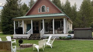 Ein zweistöckiges Haus mit Veranda, weißen Adirondack-Stühlen und einer Holzterrasse.