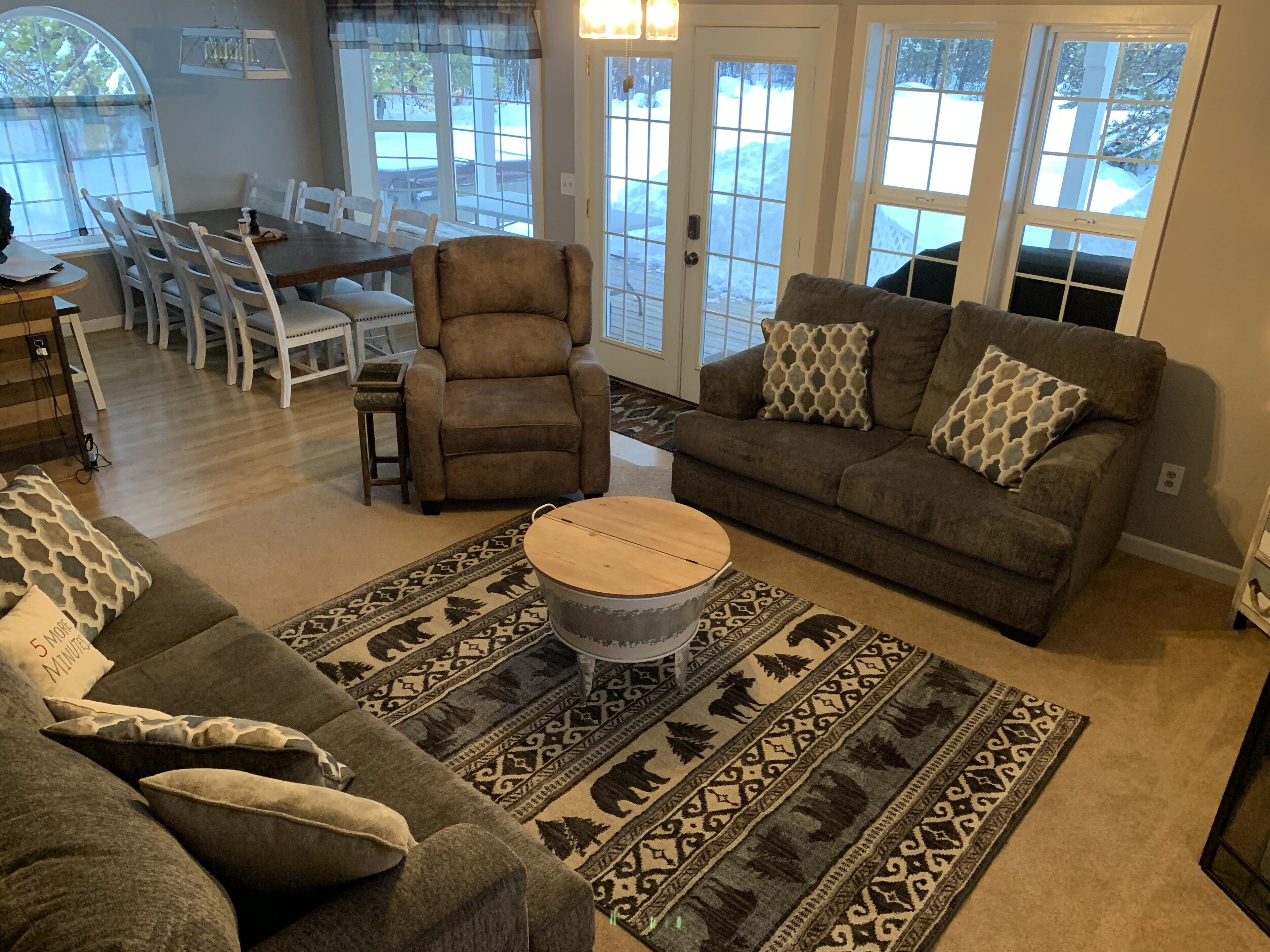 A living room with a brown sofa, a patterned rug, and a dining area with a table and chairs.