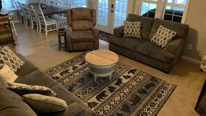 Ein Wohnzimmer mit einem braunen Sofa, einem gemusterten Teppich und einem Essbereich mit Tisch und Stühlen.