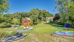 Ein Ferienhaus am See mit rotem Holzhaus, Kajaks und einer Rasenfläche mit Liegestühlen.