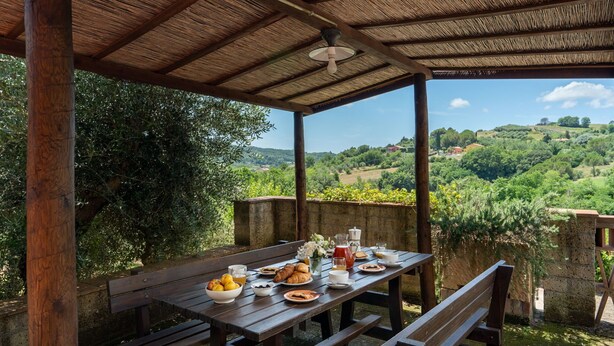 Mesa de madera al aire libre con alimentos para el desayuno, con vistas a un valle exuberante.