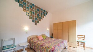A bedroom with a bed, a wooden wardrobe, a small table, and a chair.