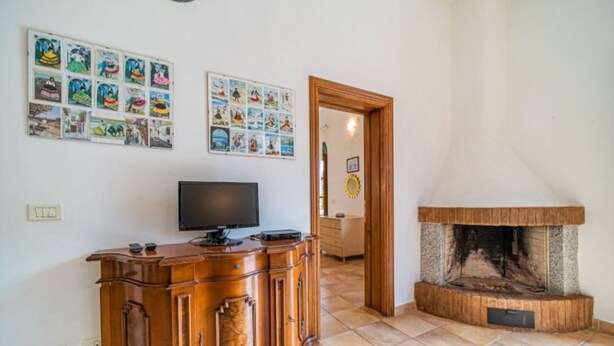 A living room with a fireplace, a television on a wooden cabinet, and various framed pictures on the wall.