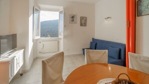 Une pièce comprenant une table à manger, des chaises, un canapé, un téléviseur et une fenêtre donnant sur les montagnes.