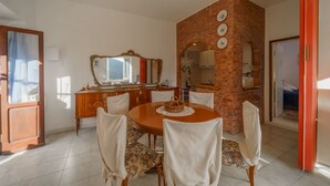 Un coin repas avec une table ronde en bois, six chaises, un miroir et un mur en briques.