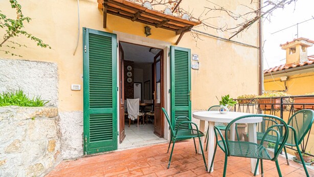 Une terrasse avec une table et des chaises, une porte donnant sur une pièce intérieure et un petit balcon agrémenté de plantes en pot.