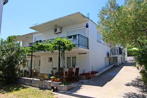 Ein zweistöckiges Gebäude mit Balkon, Sitzbereich im Freien und einem Schild mit der Aufschrift 'APARTMANI'.