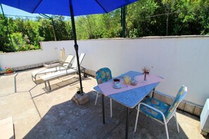 Eine Terrasse im Freien mit Tisch, Stühlen und einem blauen Sonnenschirm.