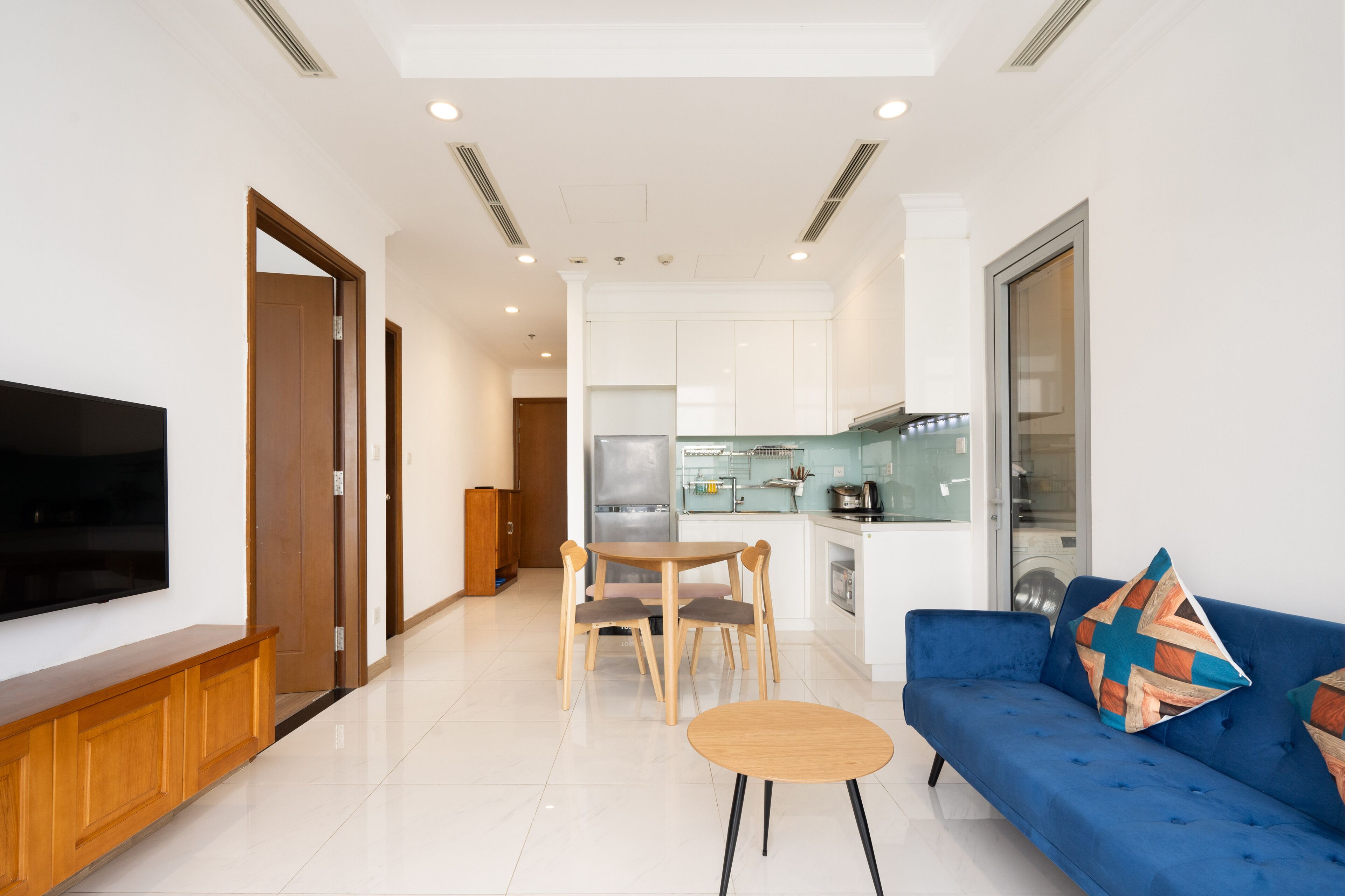 A modern living room with a flat-screen TV, a blue sofa, and a wooden dining table.