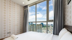 A hotel room with a large bed, a view of the cityscape through a large window, and a patterned wallpaper.