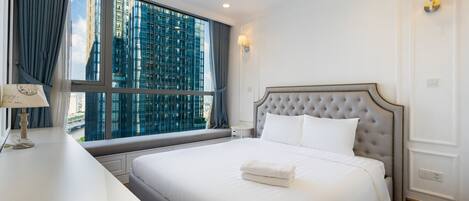 Habitación de hotel con una cama grande, una mesita de noche con lámpara, una ventana con cortinas y vistas a edificios altos.