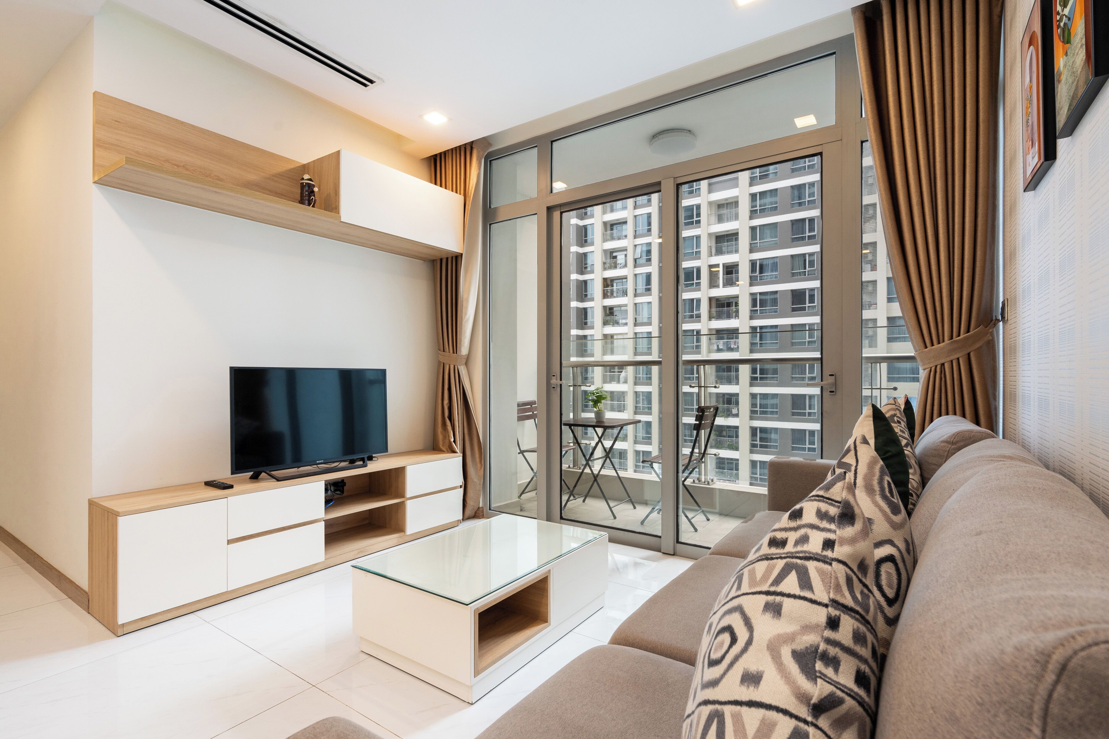 A modern living room with a flat-screen TV, a glass coffee table, and a sofa.