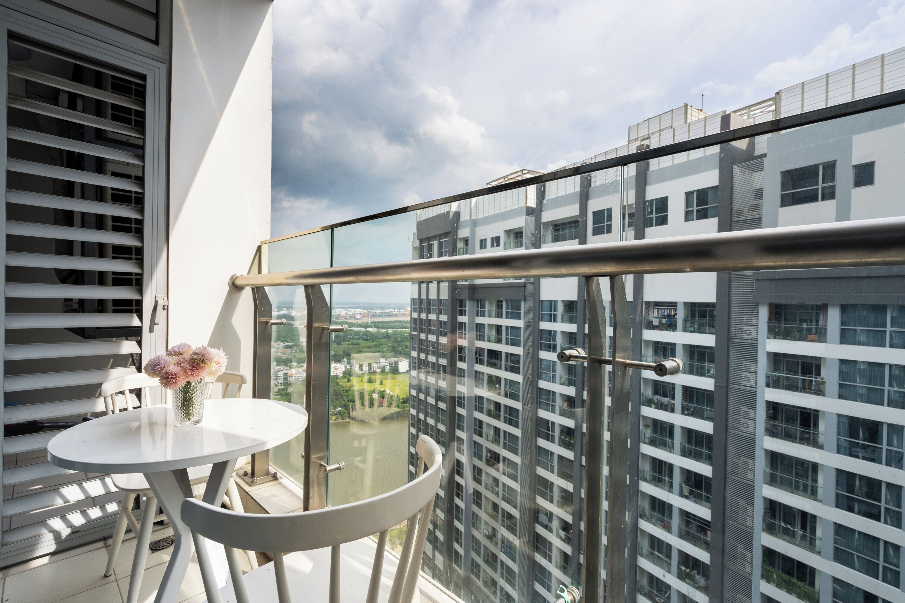 A balcony with a glass railing, a white table with chairs, and a vase of flowers.