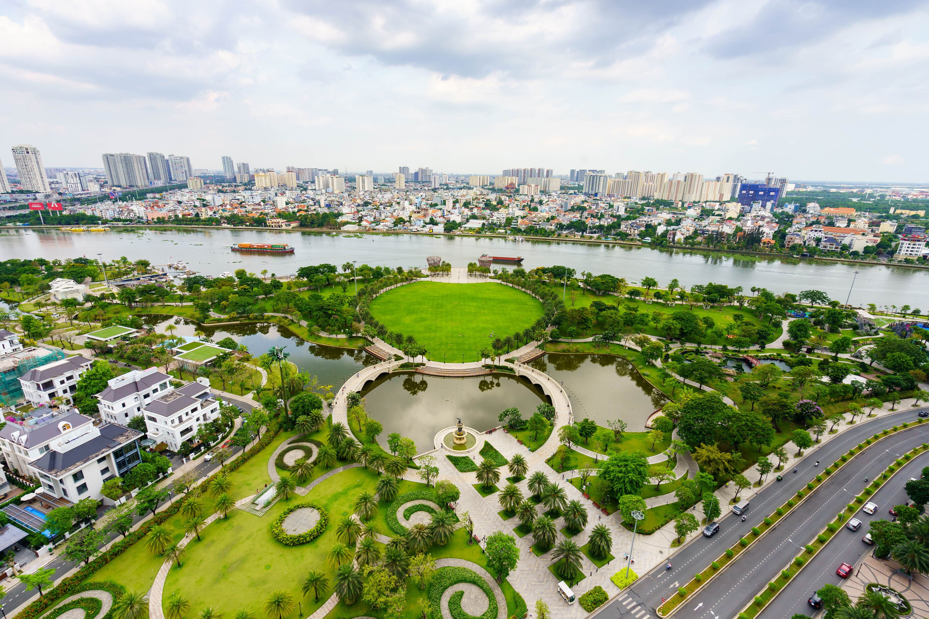 A park with a central lawn, surrounding water features, and a road with vehicles.
