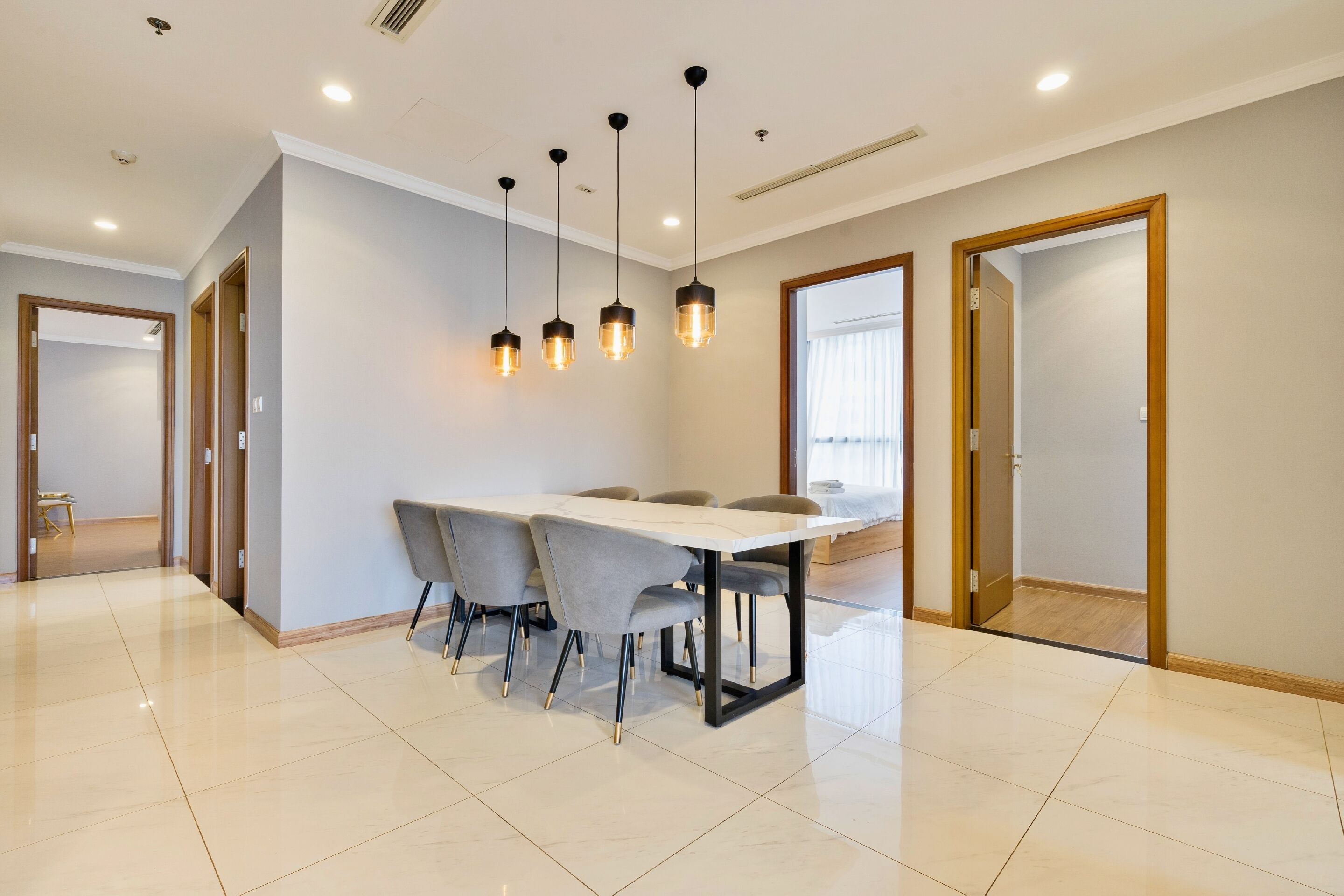 A modern dining area with a rectangular table, six grey chairs, and pendant lighting.