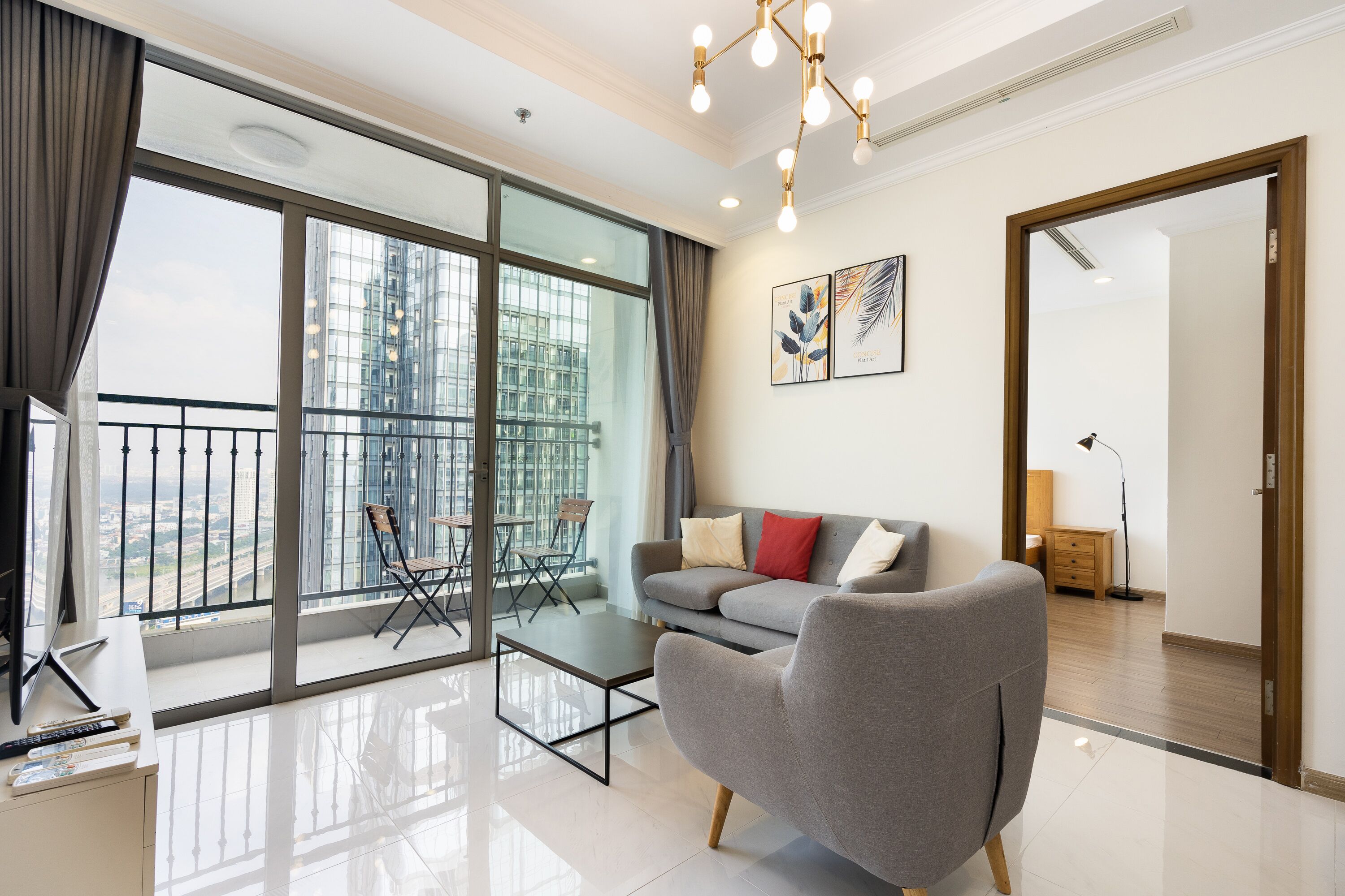 Een moderne woonkamer met een grijze bank, een glazen eettafel en een balkon met uitzicht op de stad.