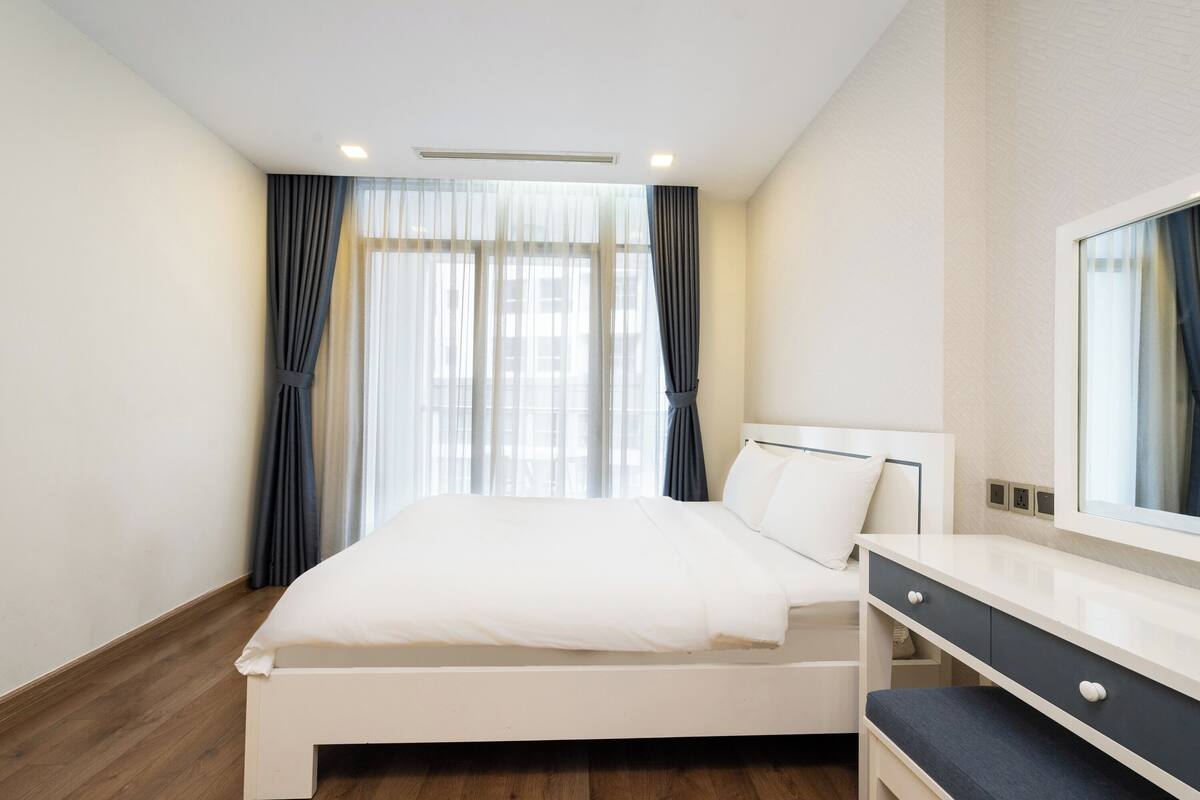 Et moderne hotelværelse med en hvid seng, et natbord, et spejl og et vindue med gardiner.