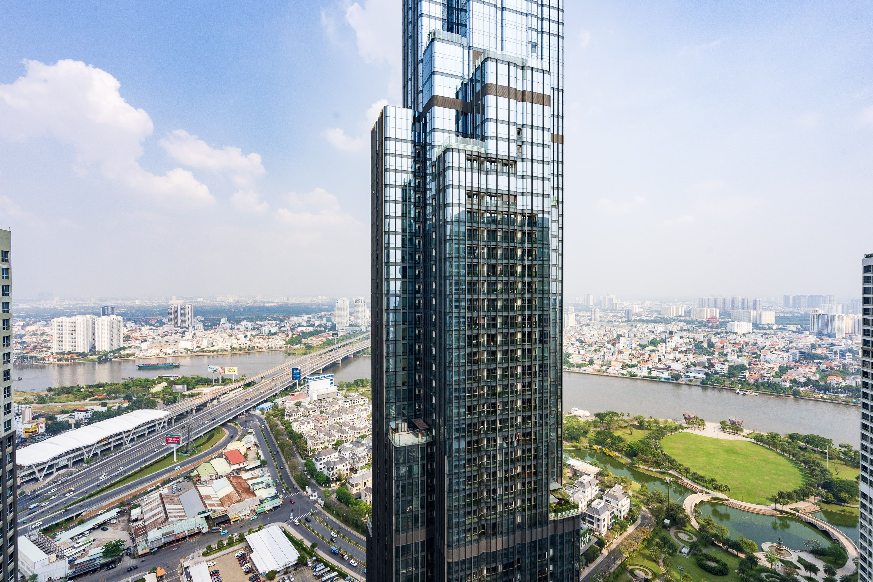 A modern high-rise building with a glass facade, surrounded by a cityscape, a river, and a park.