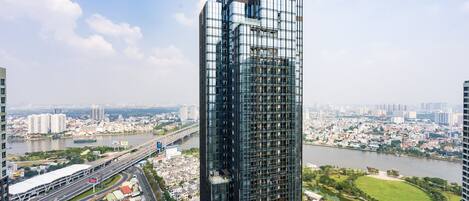 A modern high-rise building with a glass facade, surrounded by a cityscape, a river, and a park.