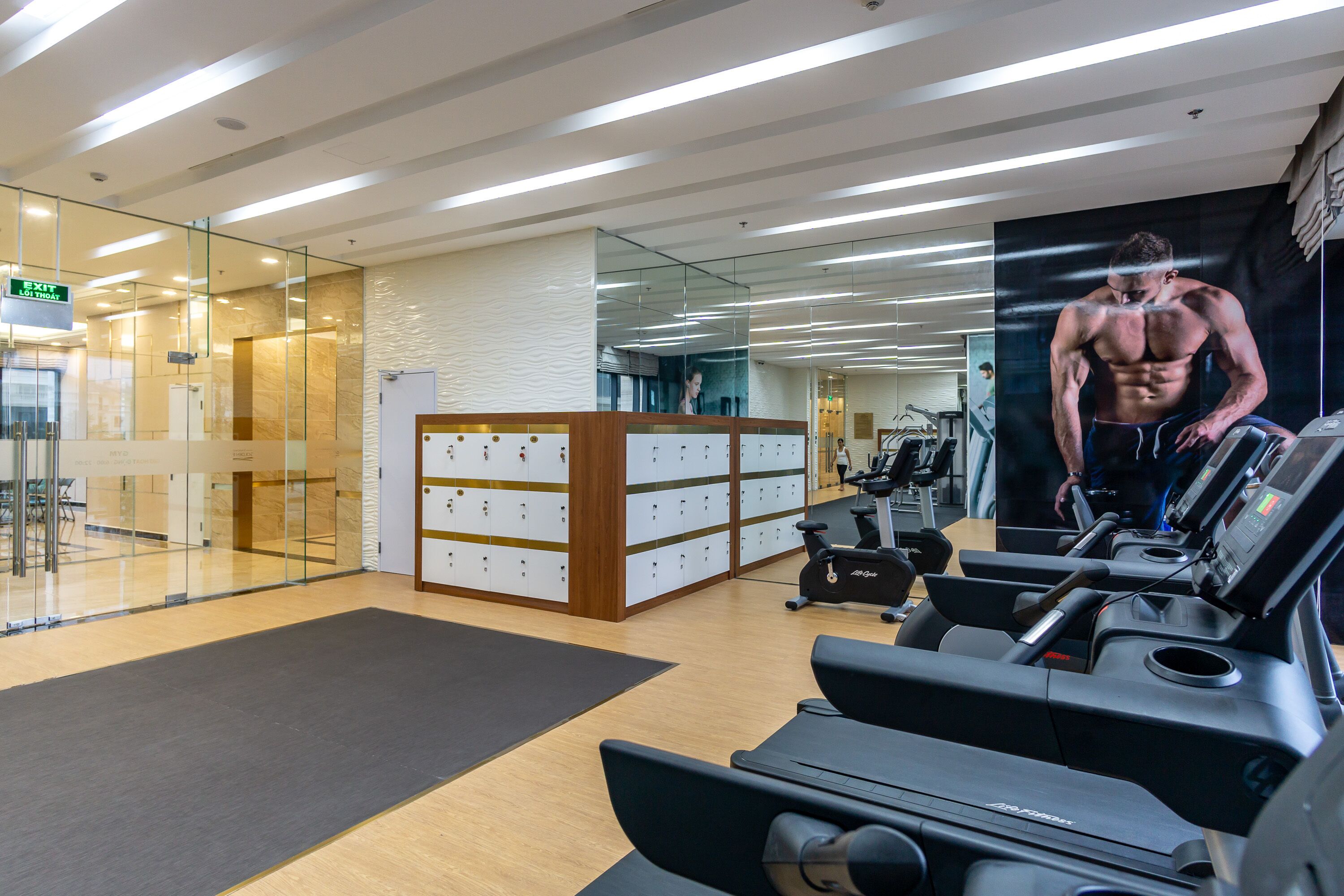 Ein modernes Fitnessstudio mit Trainingsgeräten, einem großen Spiegel und einer an der Wand befestigten Umkleide.