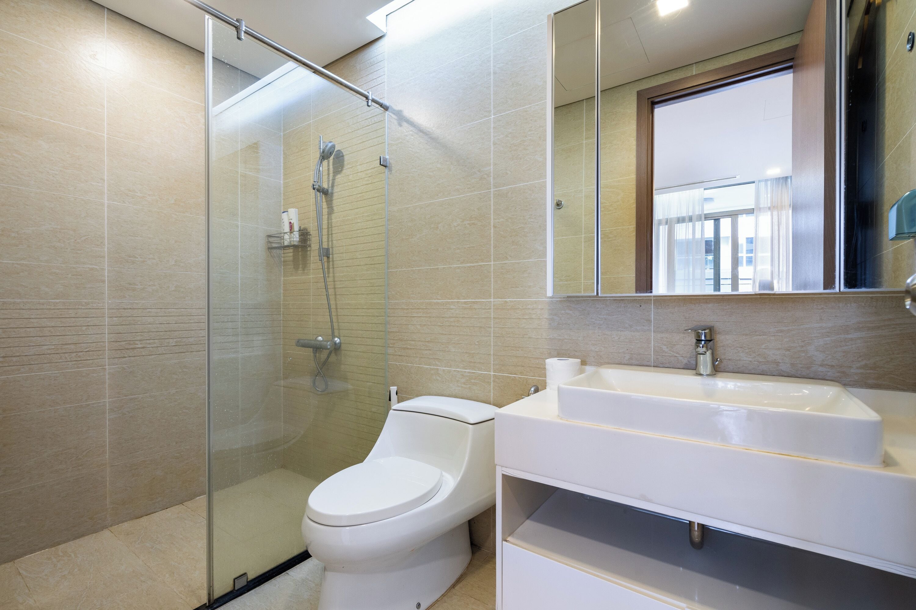 Un baño moderno con cabina de ducha de vidrio, inodoro y lavamanos blanco con espejo superior.