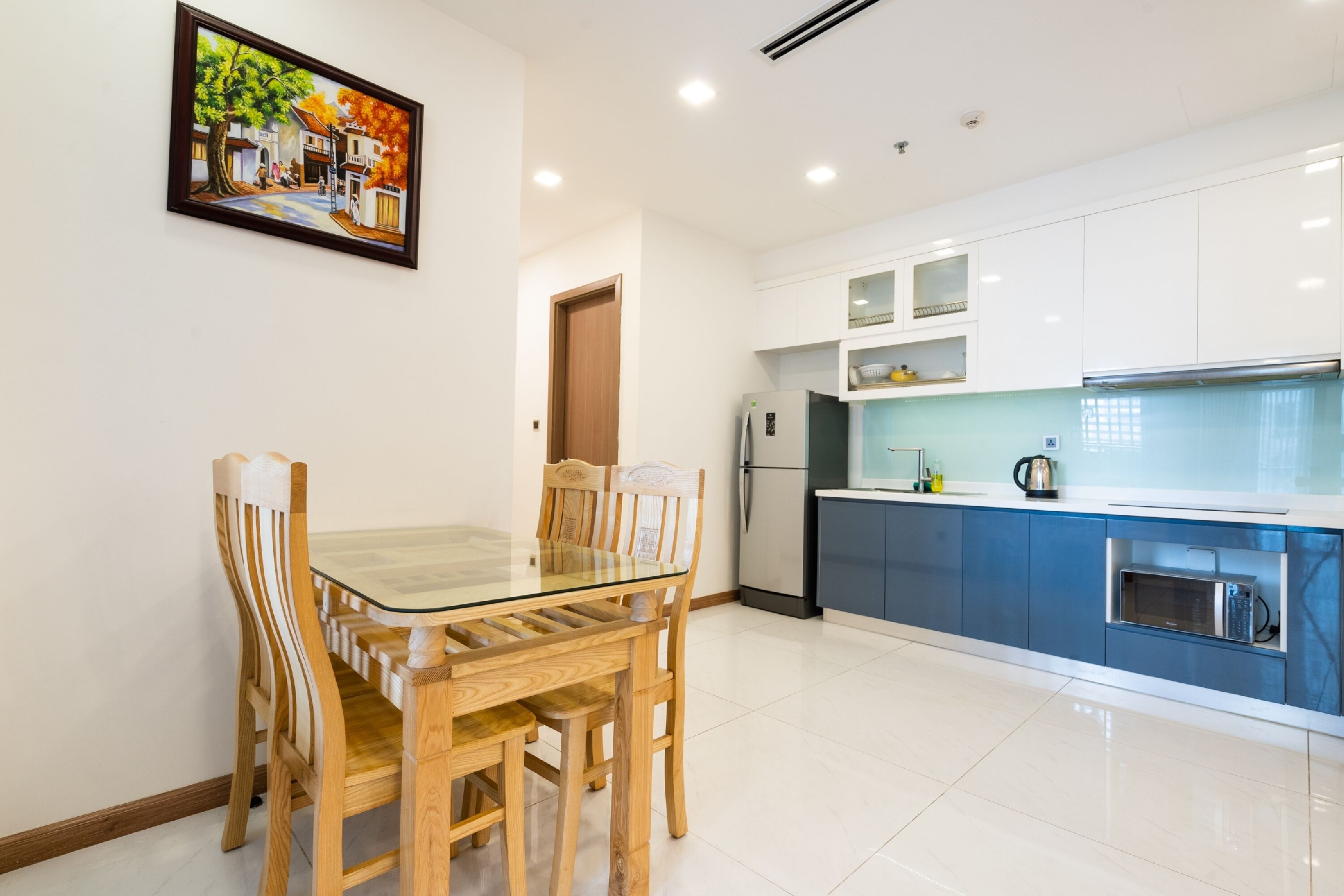 A modern kitchen with white cabinets, a blue countertop, and a glass dining table with wooden chairs.
