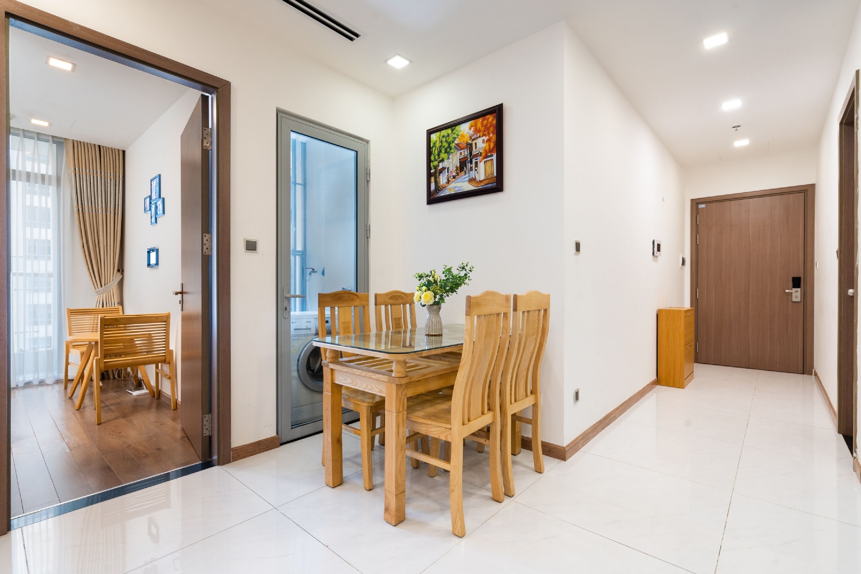 A modern dining area with a glass table and wooden chairs, a wooden cabinet, and a painting on the wall.