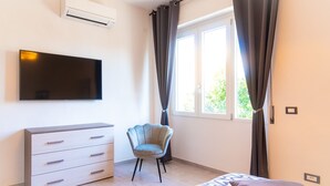 Ein Schlafzimmer mit einem Bett, einem Schminktisch, einem Sessel, einem Fernseher und einem Fenster mit Vorhängen.
