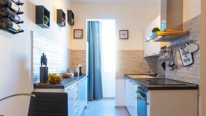 Eine moderne Küche mit Einbauofen, Spüle und Essbereich mit einem Stuhl. An der Wand stehen Weinflaschen und auf der Arbeitsfläche ein Grünpflanz.'