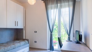 Ein modernes Schlafzimmer mit Bett, Fernseher und einem Balkon mit Vorhängen.