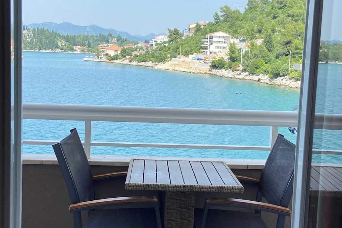 Un balcon avec une table et des chaises donnant sur une étendue d’eau et une zone côtière.