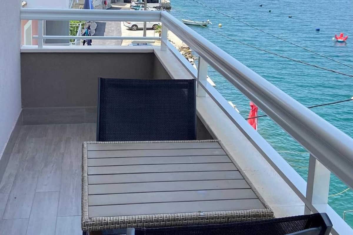 Un balcon avec une table et des chaises donnant sur une zone côtière, avec des bâtiments et des bateaux.