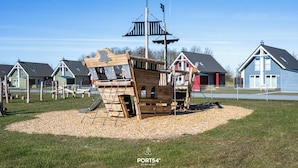 Un parque infantil con una estructura de juegos con forma de barco pirata, rodeado de casas.