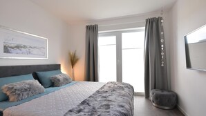 Un dormitorio moderno con una cama grande, cortinas grises, una ventana y un cuadro enmarcado en la pared.