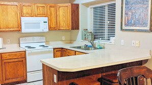 A kitchen with wooden cabinets, a white stove, a microwave, and a dining area with a table and chairs.