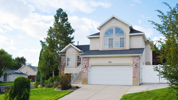 A two-story house with a garage, a front yard with a lawn and a small tree, and a driveway leading to the garage.