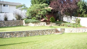 A residential property with a stone retaining wall, a well-maintained lawn, and a variety of trees including a large one with purple leaves.